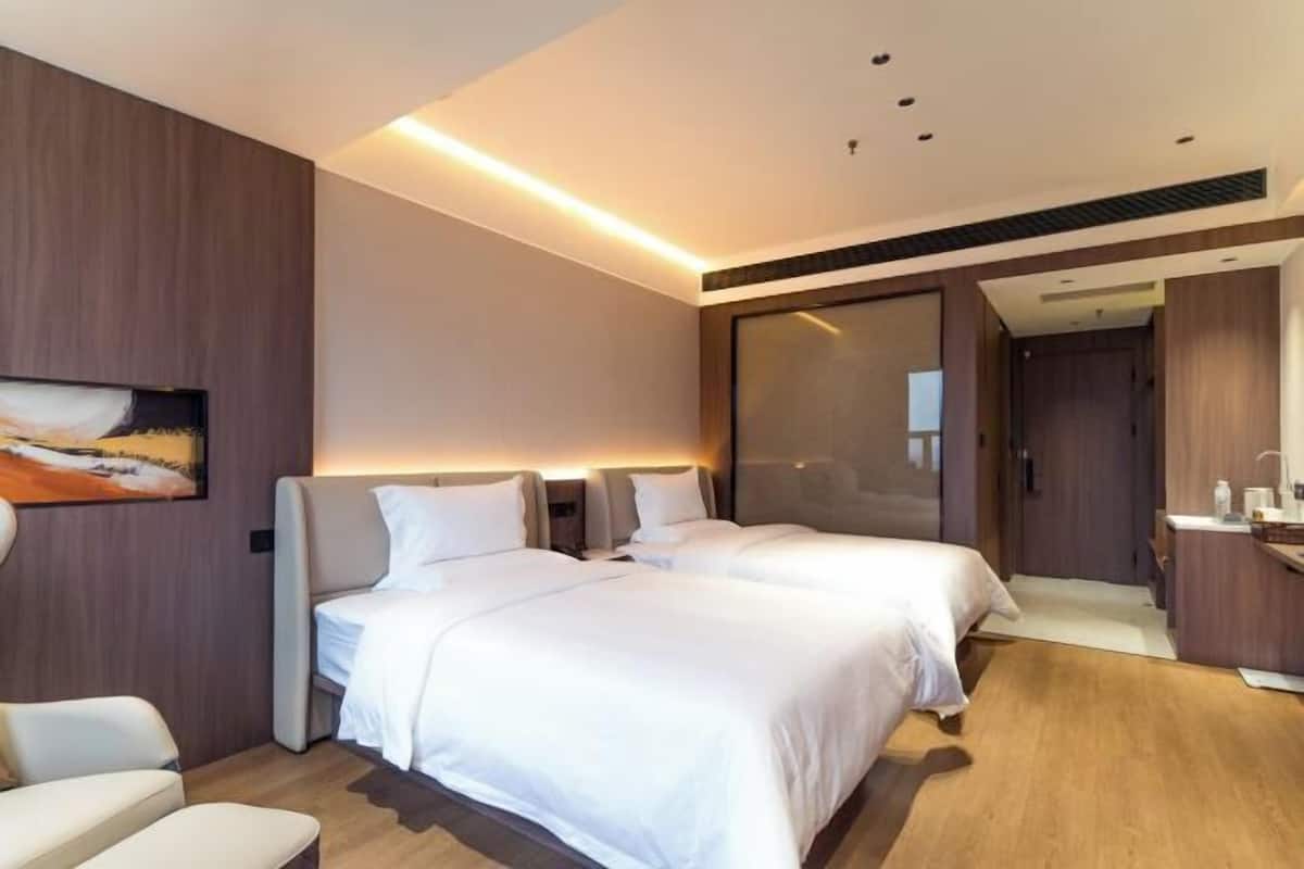 A modern hotel room with two beds, a sofa, a desk, and a bathroom.