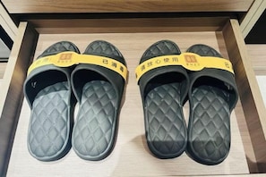 Un cajón con cuatro pares de zapatillas de estar por casa negras acolchadas y tiras amarillas.