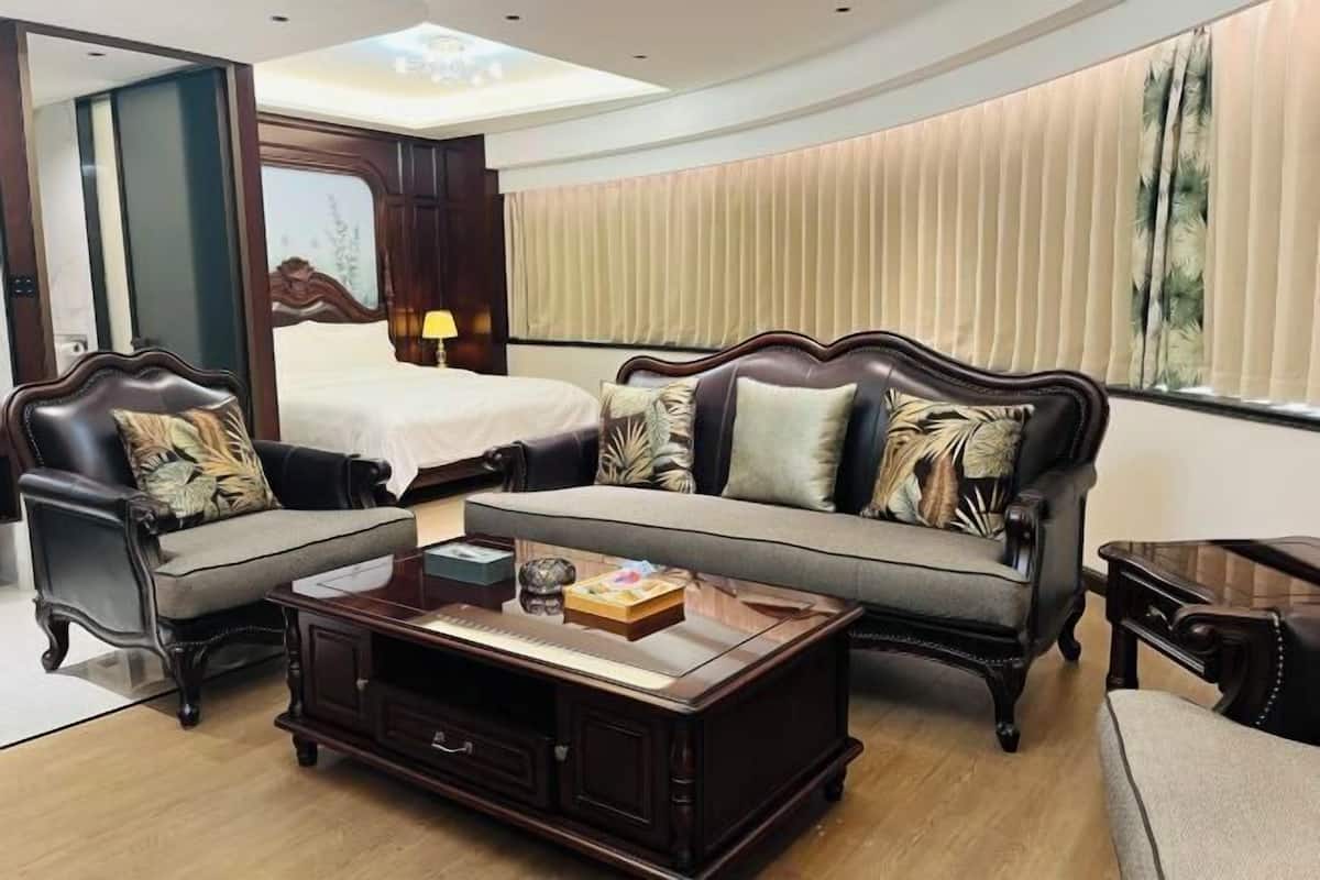 A hotel room with a bed, two armchairs, a sofa, a coffee table, and a window with curtains.