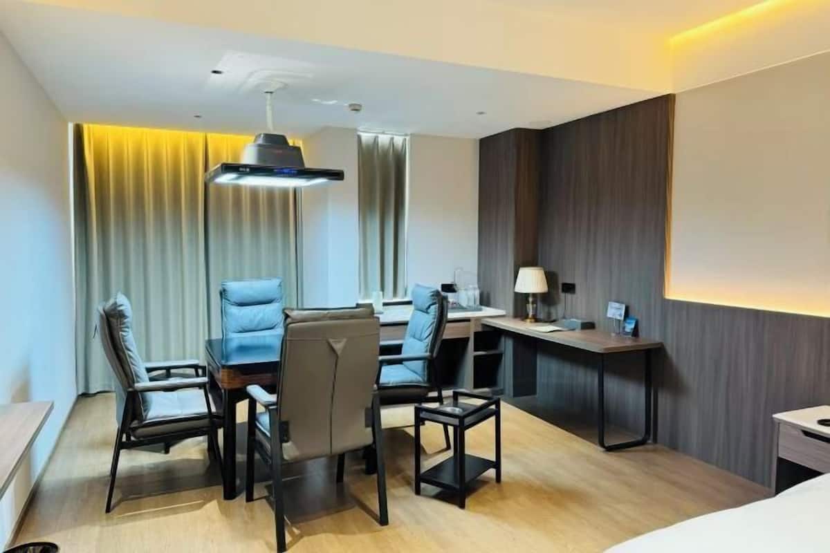 A hotel room with a desk, two chairs, a small table, a lamp, and a bed.
