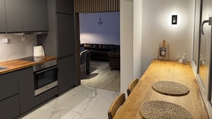 Une cuisine moderne avec des meubles de couleur sombre, un réfrigérateur en acier inoxydable et un plan de travail en bois.