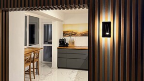 A modern kitchen with a wooden accent wall, a dining area with a table and chairs, and a painting on the wall. - Top floor private app sea & city view Balcony barbecue. Best location Chayka.  (Varna)