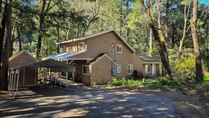 Eine zweistöckige Holzhütte mit überdachter Veranda und einer separaten Garage, umgeben von dichtem Wald.