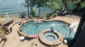 Une piscine avec un jacuzzi, entourée de chaises longues et de parasols, offrant une vue sur un lac.