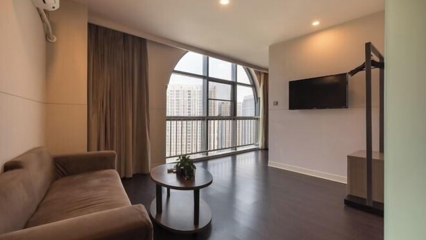 A modern living room with a large window, a flat-screen TV, a sofa, and a small table with a plant. - Jinjiang Inn Select (Xuzhou High-speed Railway Huaihai Huanqiugang) (Xuzhou)