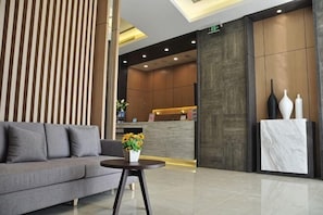 A modern reception area with a sofa, a small table with flowers, and a reception desk.