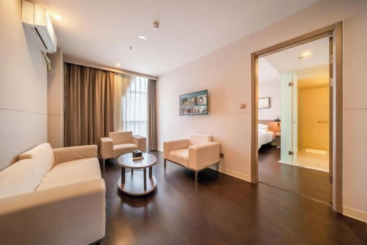 A hotel room with a sofa, two armchairs, a coffee table, a painting, and a door leading to a bathroom.
