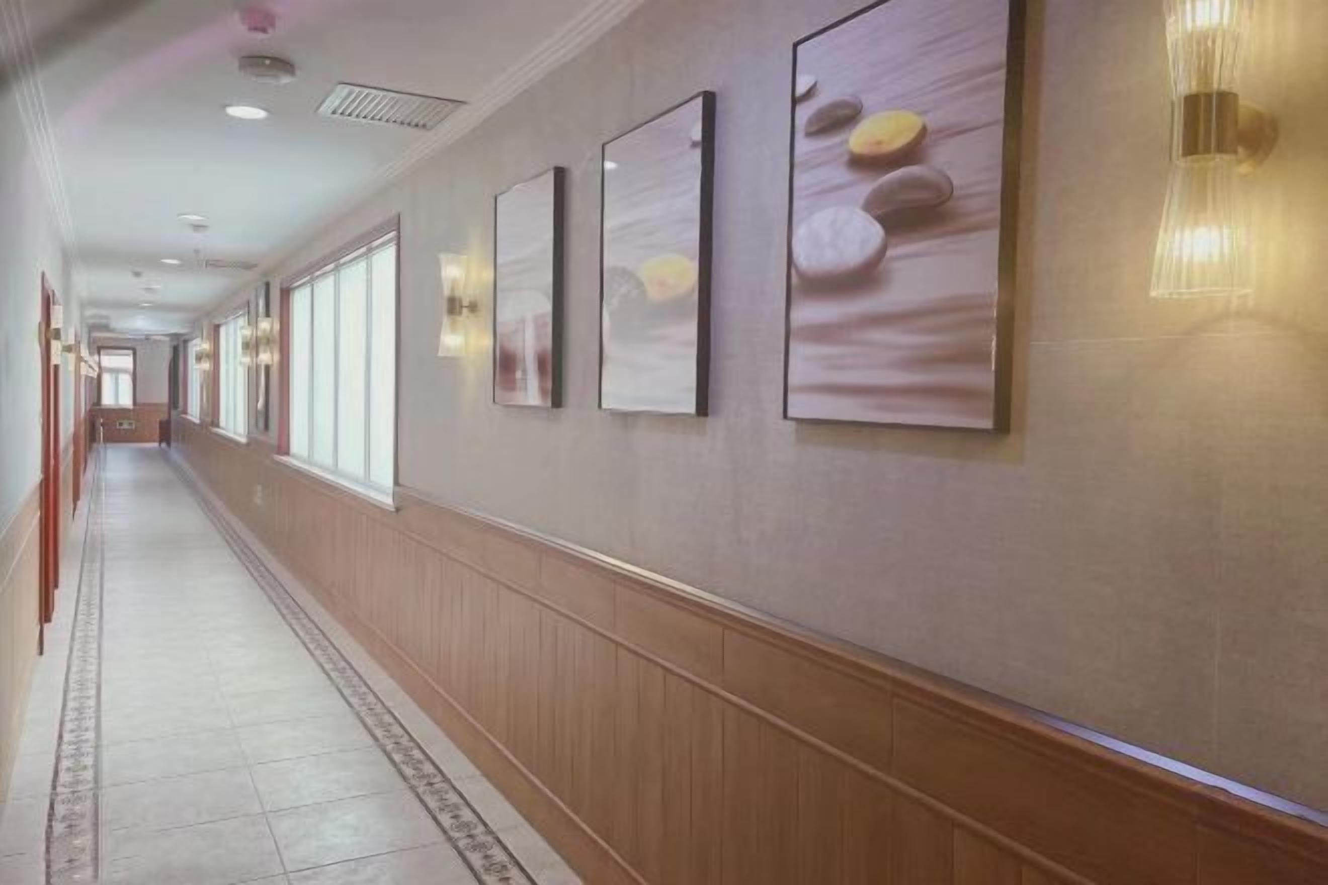A long, narrow hallway with wooden paneling, large windows, and framed artwork on the walls.