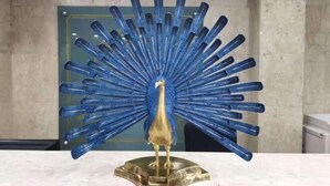 A peacock sculpture with a golden base, surrounded by blue elements, set against a marble wall with a decorative ceiling. - Shanghai Jiu Yu Hotel (Shanghai)
