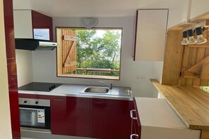 A compact kitchen with a built-in oven, a sink, and a window overlooking a wooden deck. - Chalet AYOUNAKA at sunset, panoramic view of the Caribbean Sea (Bouillante)
