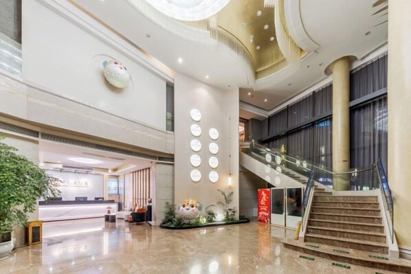 A spacious lobby with a reception desk, a staircase, and a large decorative ceiling.
