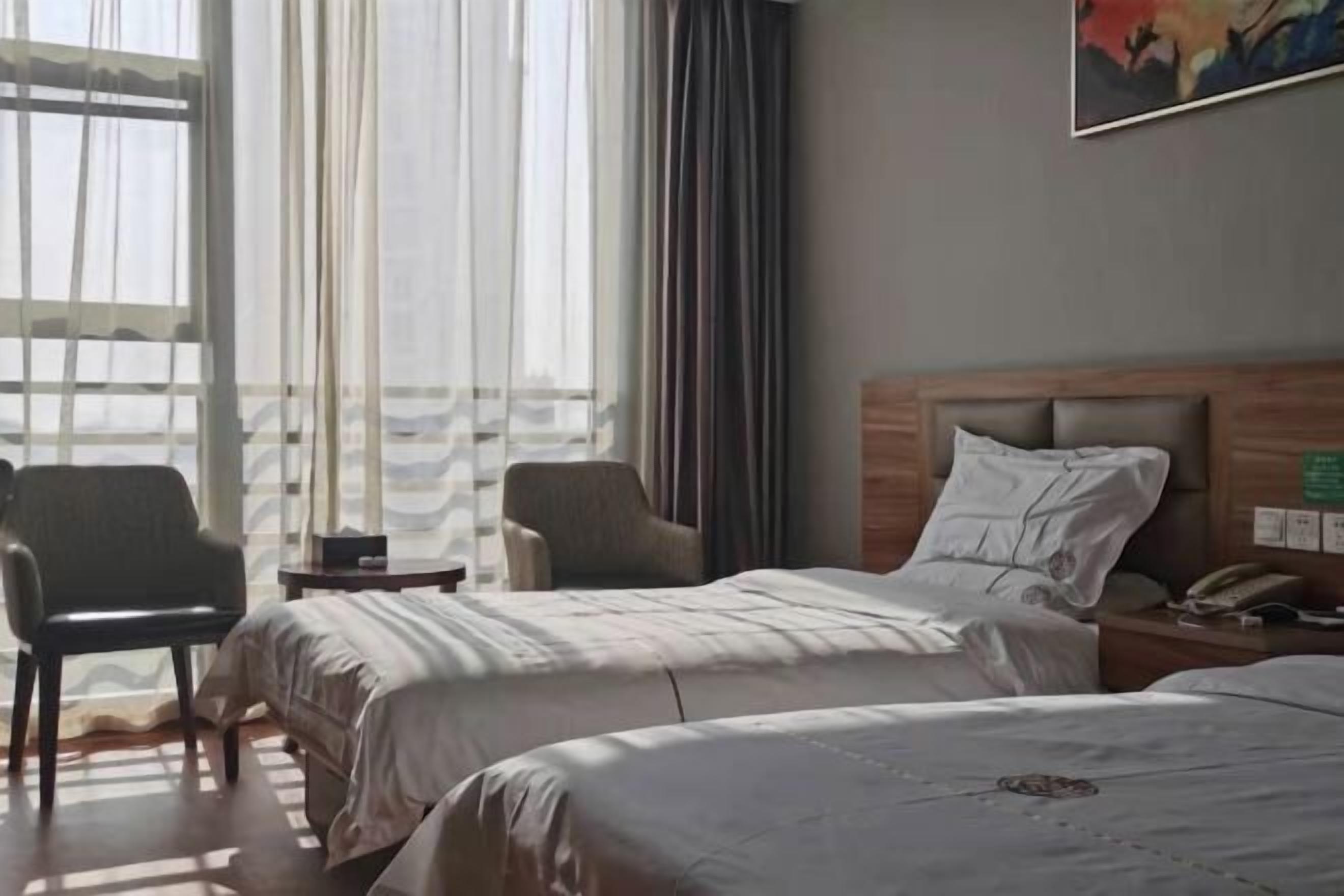 A hotel room with two beds, a chair, a small table, and a painting on the wall.