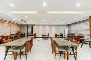 Un salón de conferencias con varias mesas y sillas, una pizarra y un ventanal grande.