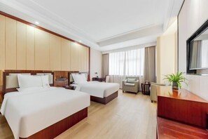 Habitación de hotel con dos camas, un escritorio, una silla y un ventanal con cortinas.