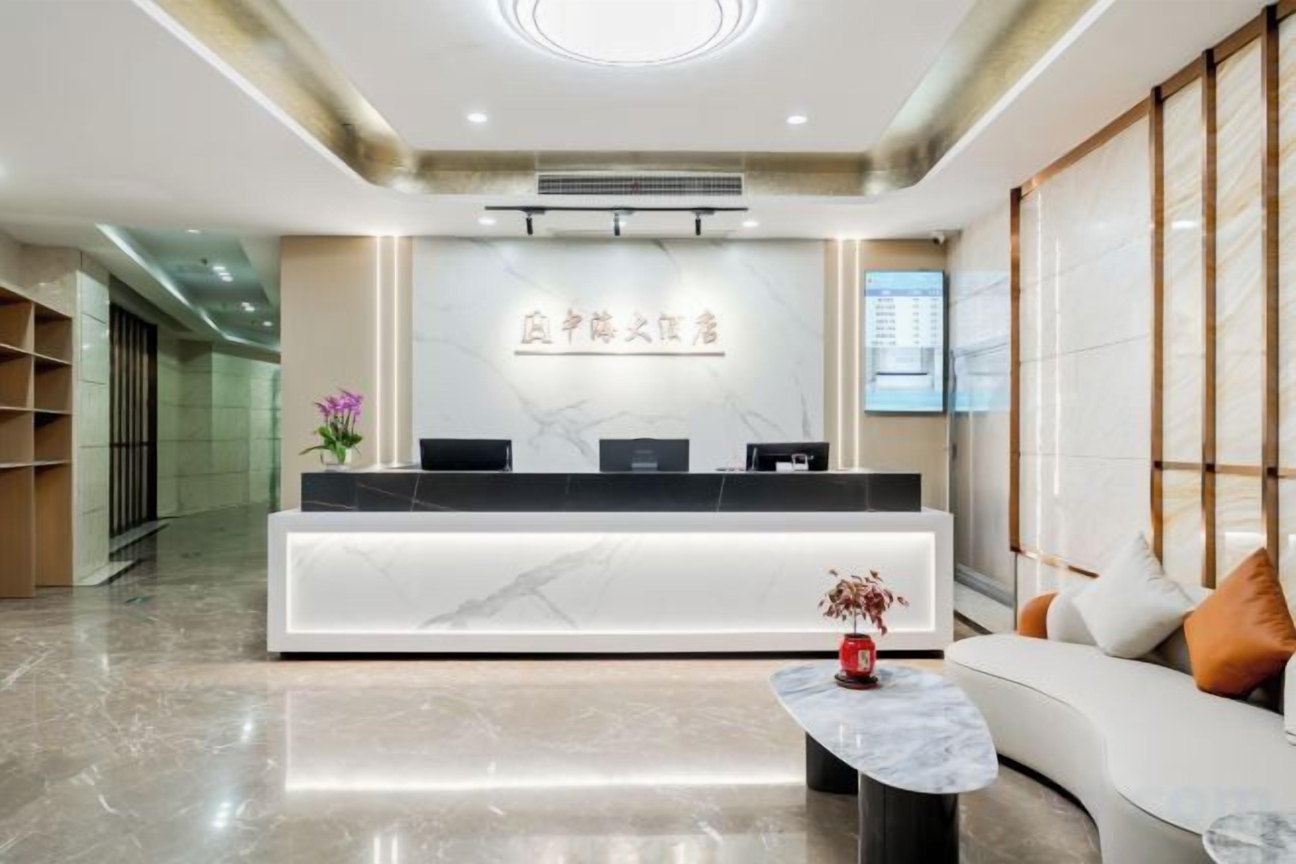 Zona de recepción de un hotel con un mostrador de mármol, un sofá con cojines, una mesita con un jarrón y un equipo de aire acondicionado instalado en la pared.
