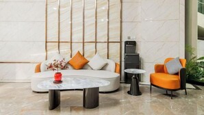 Een moderne lobby met een witte bank, een klein rond tafeltje en een oranje fauteuil.