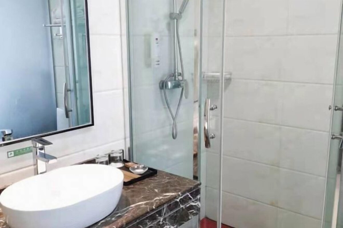 Ein modernes Badezimmer mit einem großen Spiegel, einem weißen Waschbecken und einer Duschkabine aus Glas.