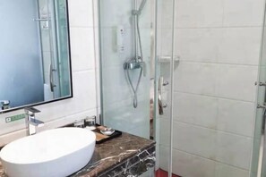 Ein modernes Badezimmer mit einem großen Spiegel, einem weißen Waschbecken und einer Duschkabine aus Glas.
