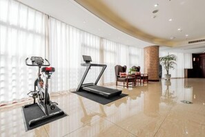 Habitación de hotel con una caminadora, un comedor con mesa y sillas, y un ventanal con cortinas.