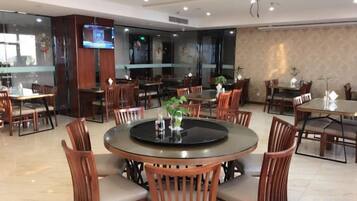 Une salle à manger d’hôtel avec des tables rondes, des chaises en bois et un écran de télévision.