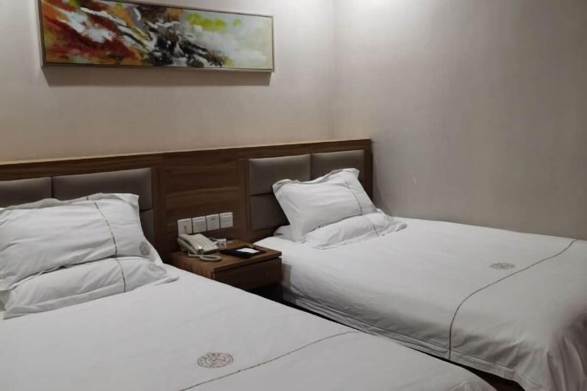 Ein Hotelzimmer mit zwei Betten, einem Nachttisch mit Telefon und Buch, sowie einem Gemälde an der Wand.