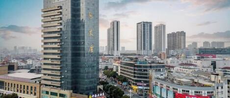 Un edificio alto con varios pisos, rodeado de otros edificios y una calle concurrida.