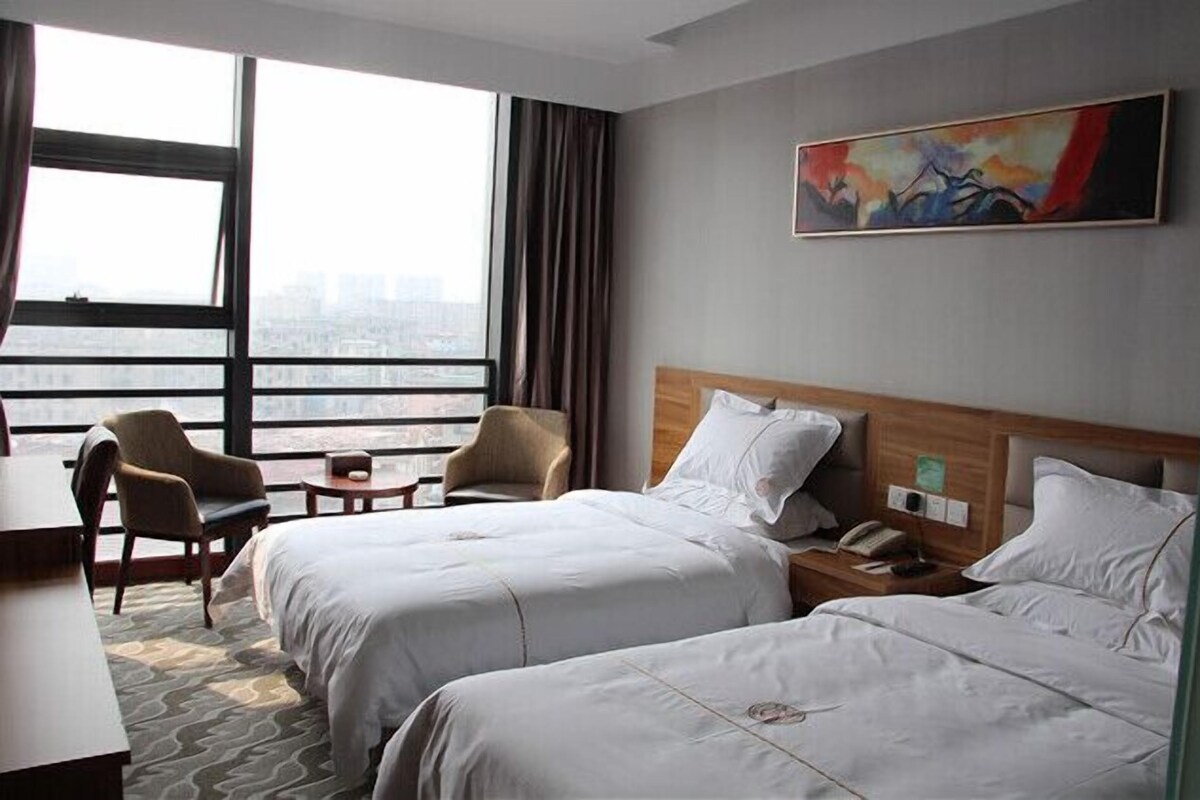Ein Hotelzimmer mit zwei Betten, einem Schreibtisch, einem Stuhl und einem großen Fenster mit Blick auf die Stadt.