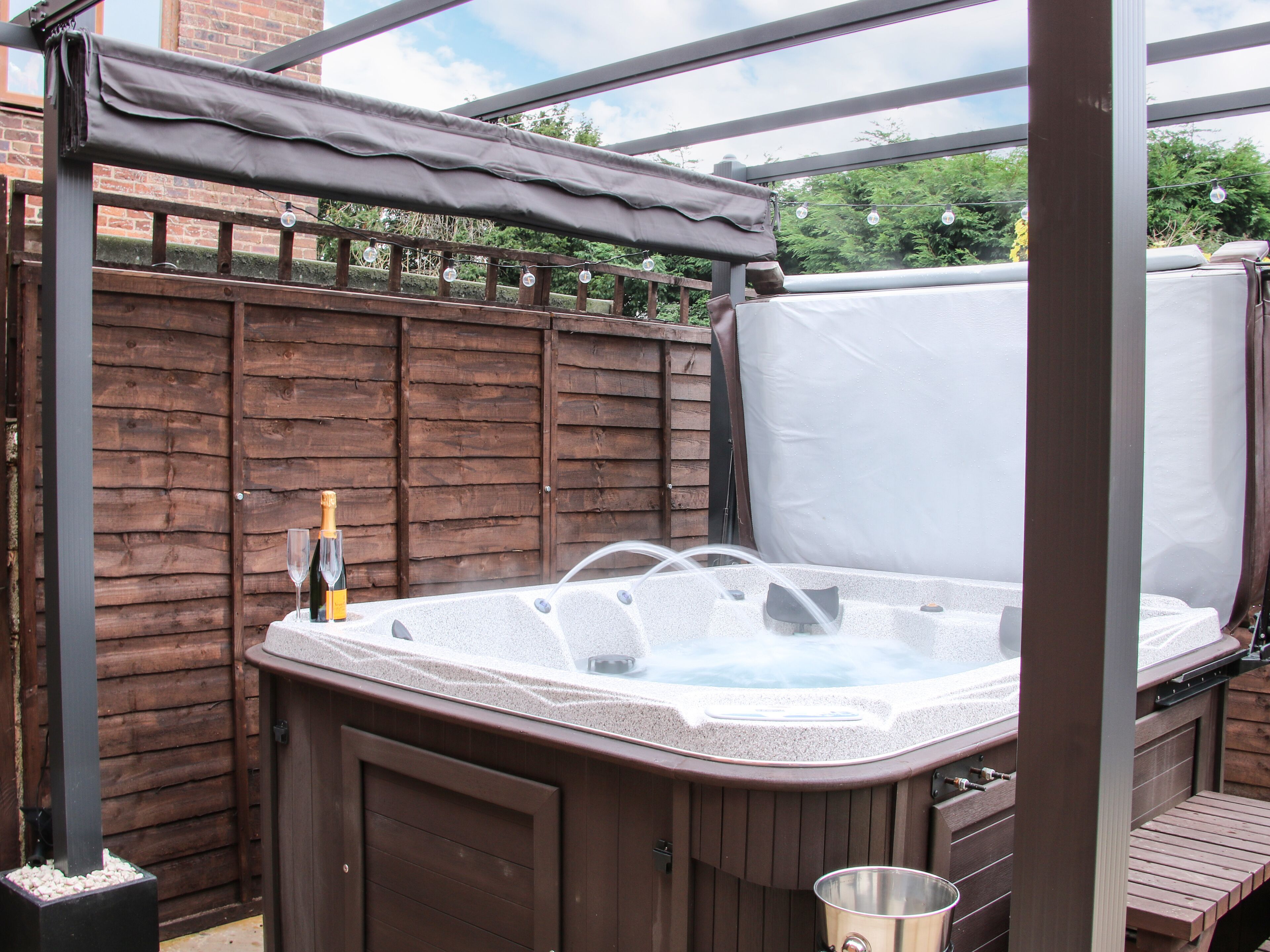 Een hottub met houten ombouw, een fles champagne en een metalen emmer.
