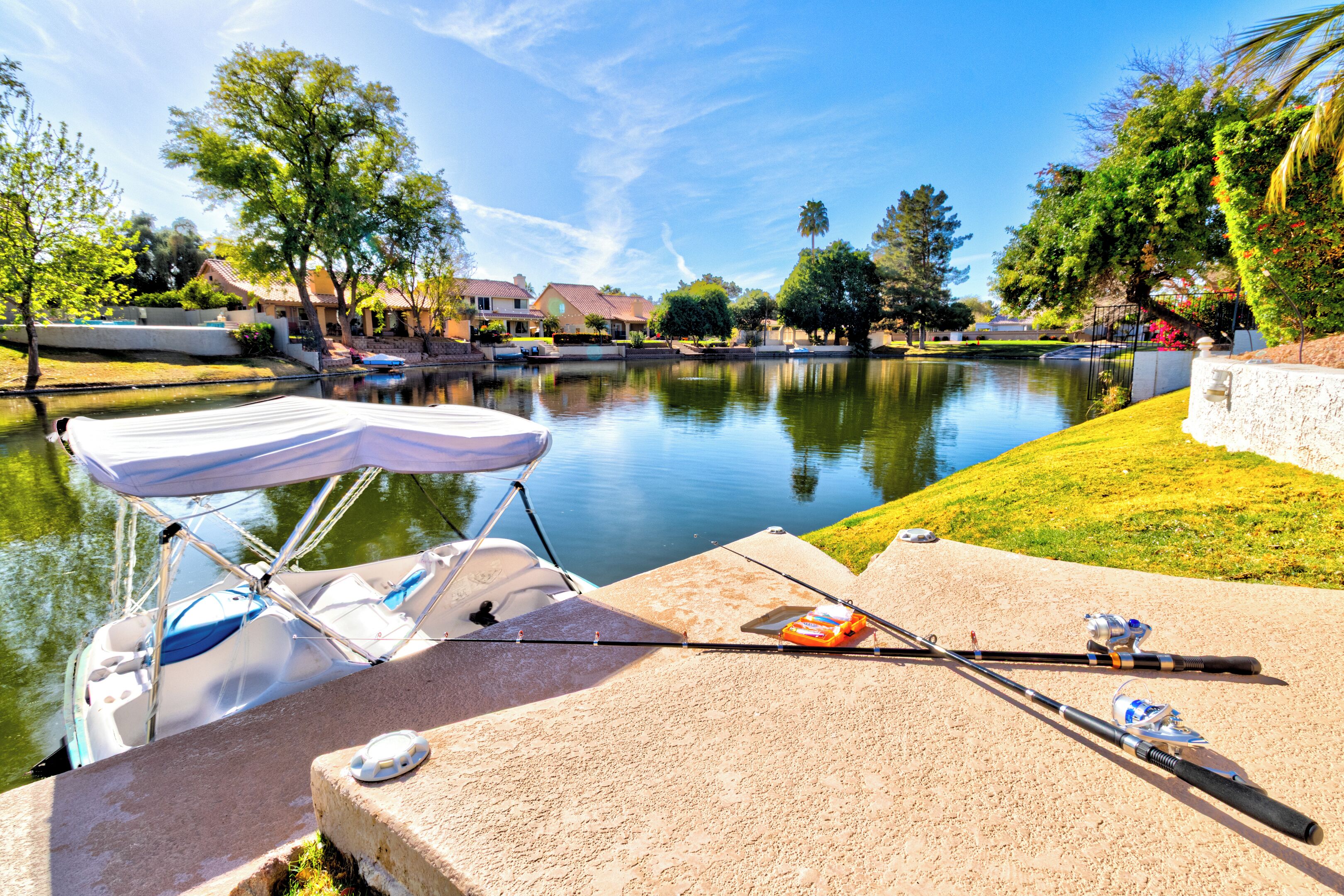 A fishing setup with a boat docked by a calm water body, surrounded by lush greenery and residential houses.