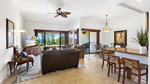 Ein geräumiger Wohnbereich mit großem Sofa, einem Esstisch mit Stühlen, einer Küchenzeile und einem Deckenventilator.
