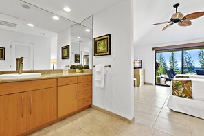 A modern bathroom with a large mirror, wooden cabinets, and a ceiling fan. - lanai beauty, soak up the sun and enjoy golf views (Lahaina)