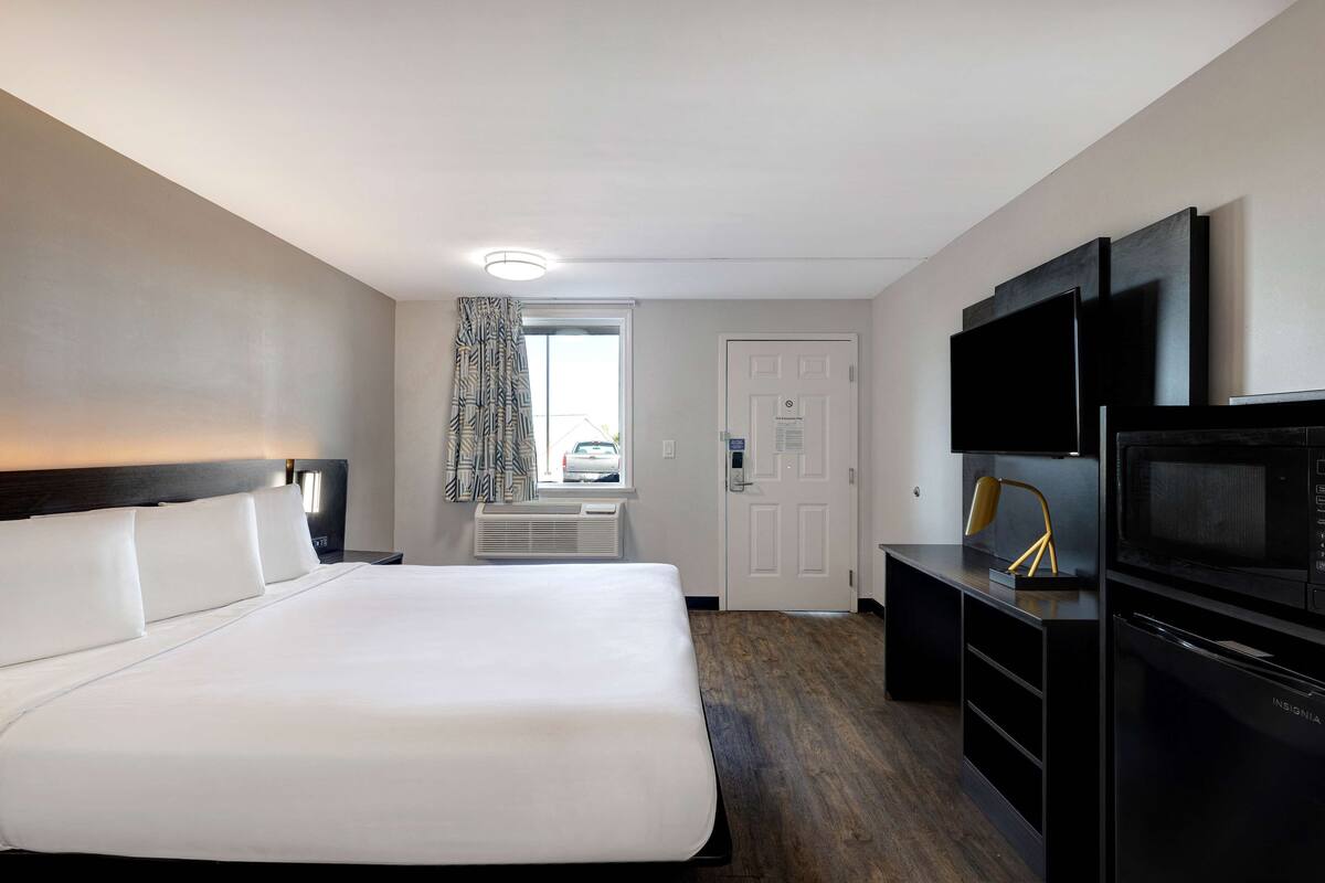 A hotel room with a large bed, a desk with a flat-screen TV, a microwave, and a door leading to a balcony.