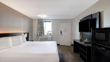 Quarto de hotel com uma cama grande, uma escrivaninha com televisão de ecrã plano, micro-ondas e porta para uma varanda.