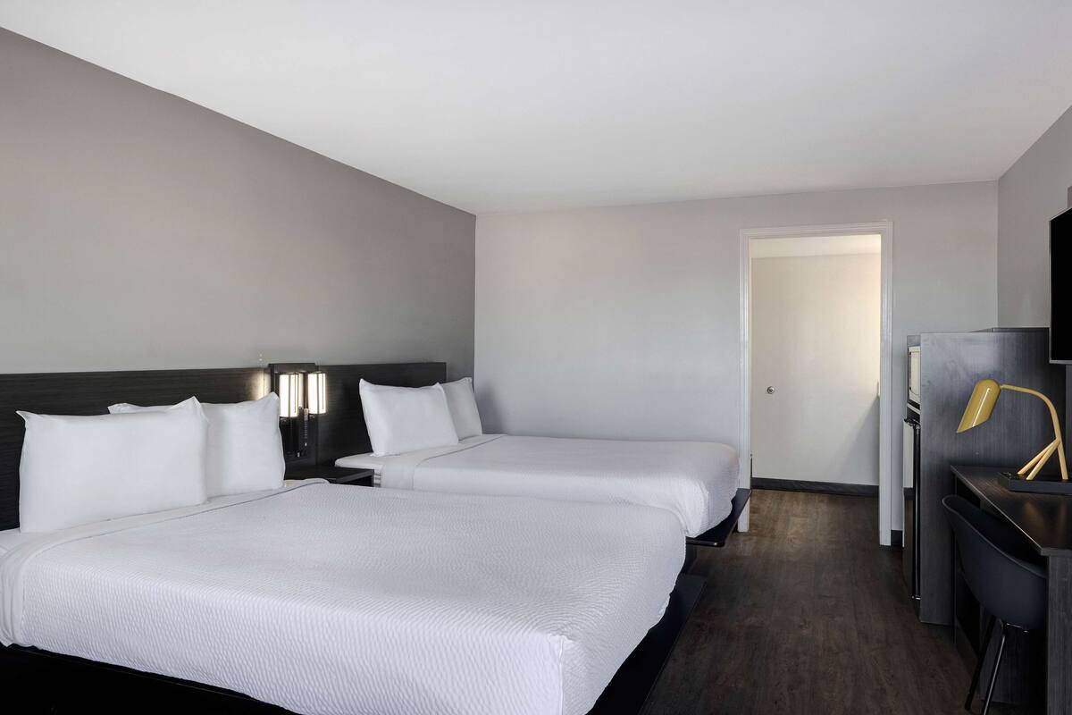 A hotel room with two beds, a desk with a chair, a TV, and a door leading to another room.