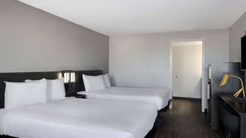 Habitación de hotel con dos camas, un escritorio con silla, televisión y una puerta que da a otra habitación.