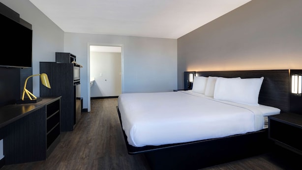 A modern hotel room with a large bed, a desk with a lamp, a TV, and a wardrobe. - Motel 6 Bonne Terre, MO (Bonne Terre)