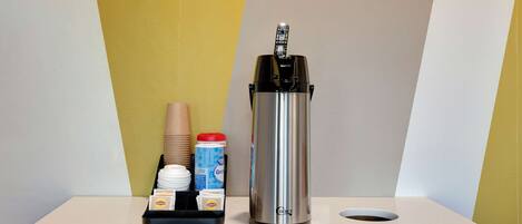 A coffee machine on a counter with disposable cups, a container of creamer, and a tray with coffee pods.
