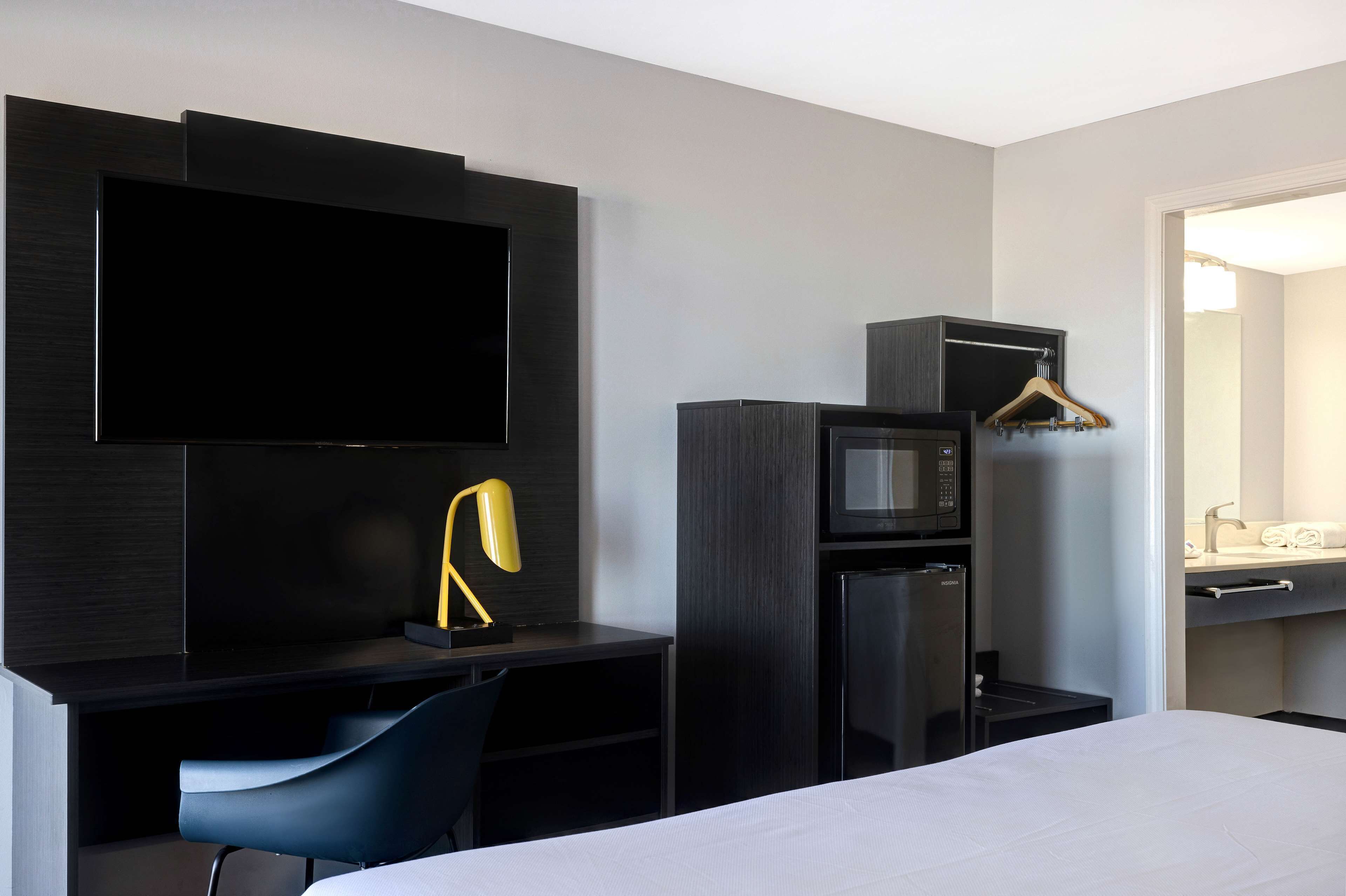 Een moderne hotelkamer met een flatscreen-tv, een bureau met stoel, een magnetron, een koelkast en een kledingrek.