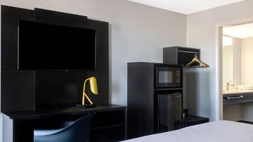 Een moderne hotelkamer met een flatscreen-tv, een bureau met stoel, een magnetron, een koelkast en een kledingrek.