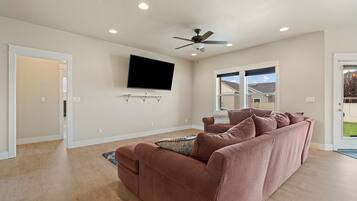 A modern living room with a large flat-screen TV mounted on the wall, a ceiling fan, and a sectional sofa.