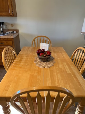 A dining area with a table set for four, featuring a decorative bowl of fruits and nuts.