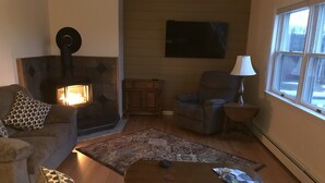 A cozy living room with a fireplace, comfortable seating, and a view of the outdoors. - Spectacular views and close to three ski areas; Stowe, Smuggler’s  and Jay Peak. (Hyde Park)