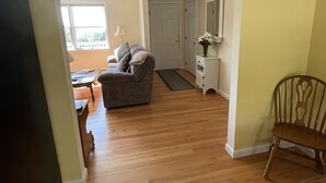 A living room with a sofa, a wooden floor, a dining table, and a chair. - Spectacular views and close to three ski areas; Stowe, Smuggler’s  and Jay Peak. (Hyde Park)
