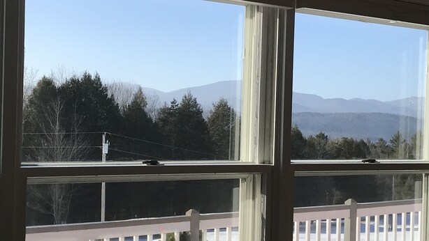 A room with two large windows overlooking a snowy deck with a white railing. - Spectacular views and close to three ski areas; Stowe, Smuggler’s  and Jay Peak. (Hyde Park)