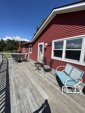 Une maison rouge avec une terrasse en bois, une table avec des chaises et un parasol rouge.