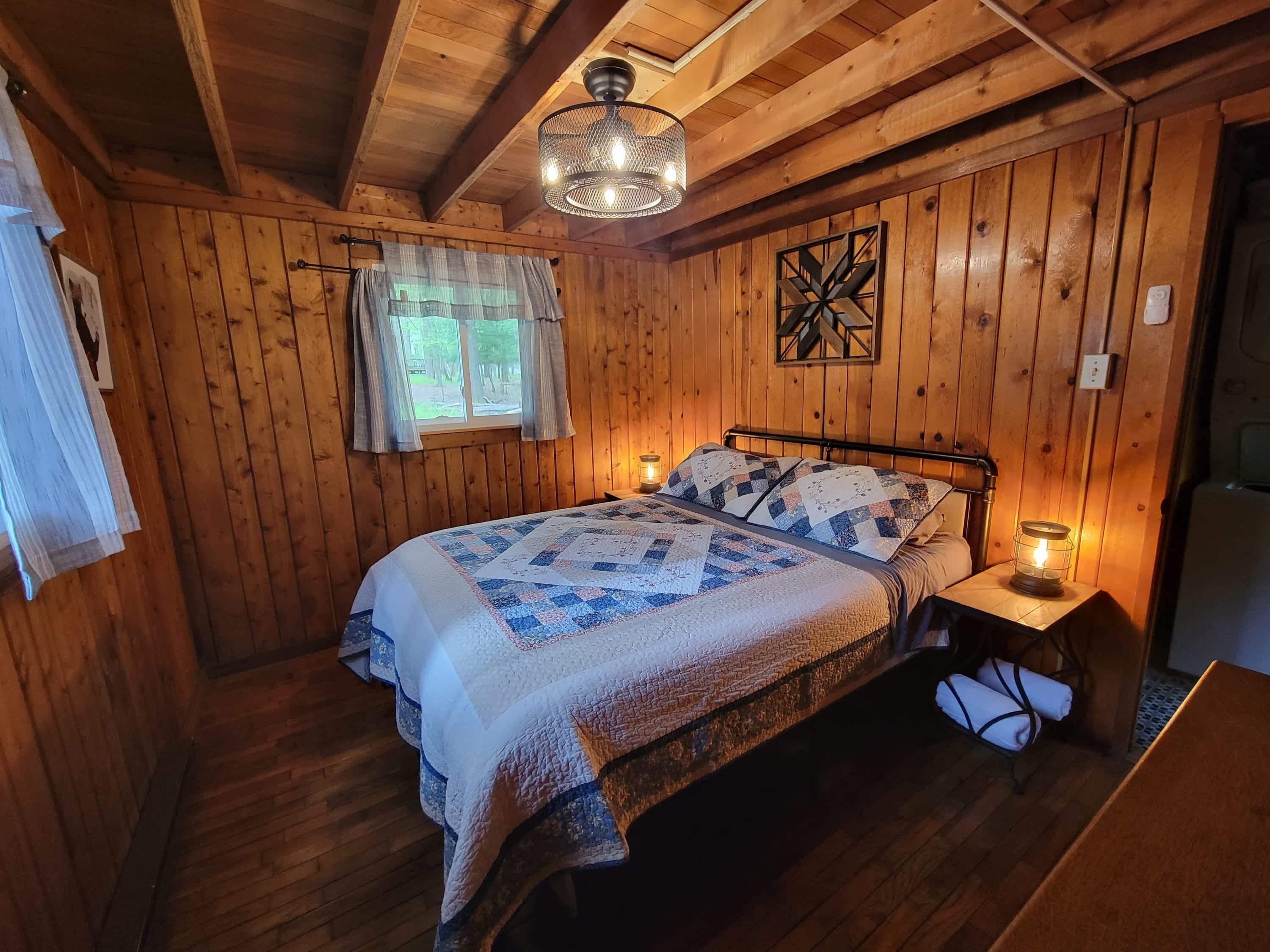 Een houten slaapkamer met een bed, een raam met gordijnen, een sterdecoratie aan de muur en een hanglamp.