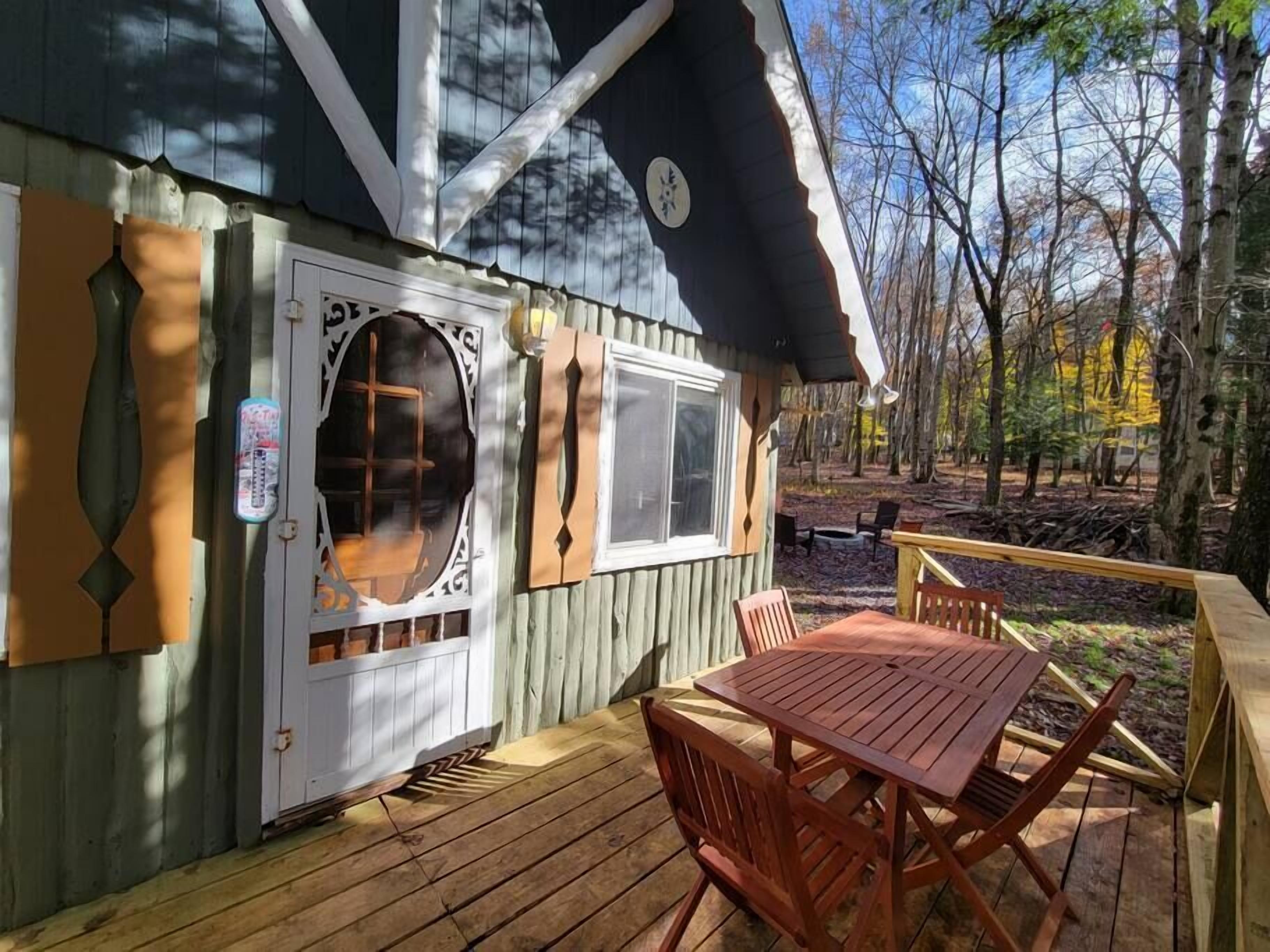 Eine Holzterrasse mit Tisch und Stühlen, ein überdachter Patio-Bereich und Blick auf ein bewaldetes Gebiet.