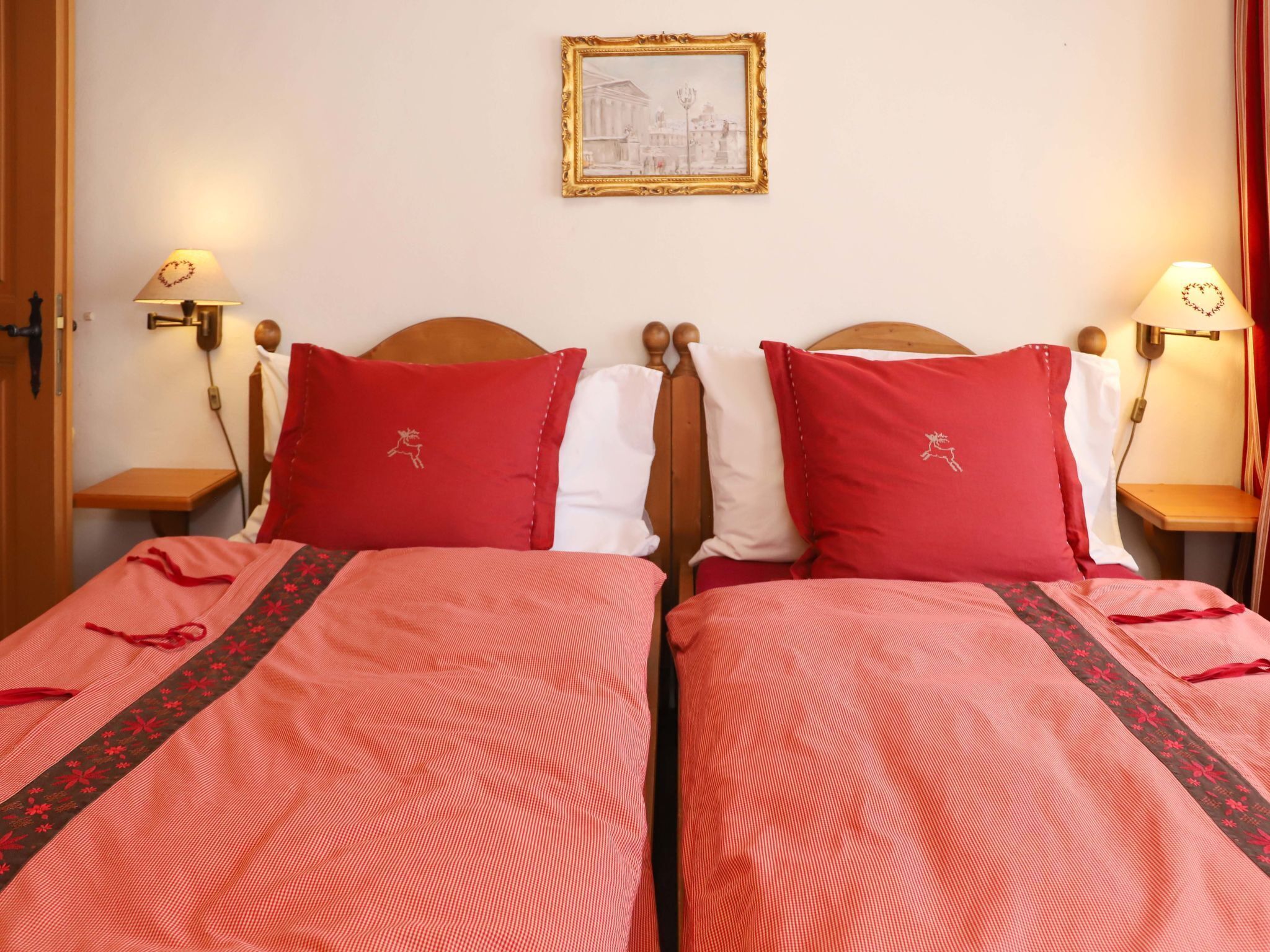 A hotel room with two beds, each with red and white bedding, a framed picture on the wall, and bedside lamps.