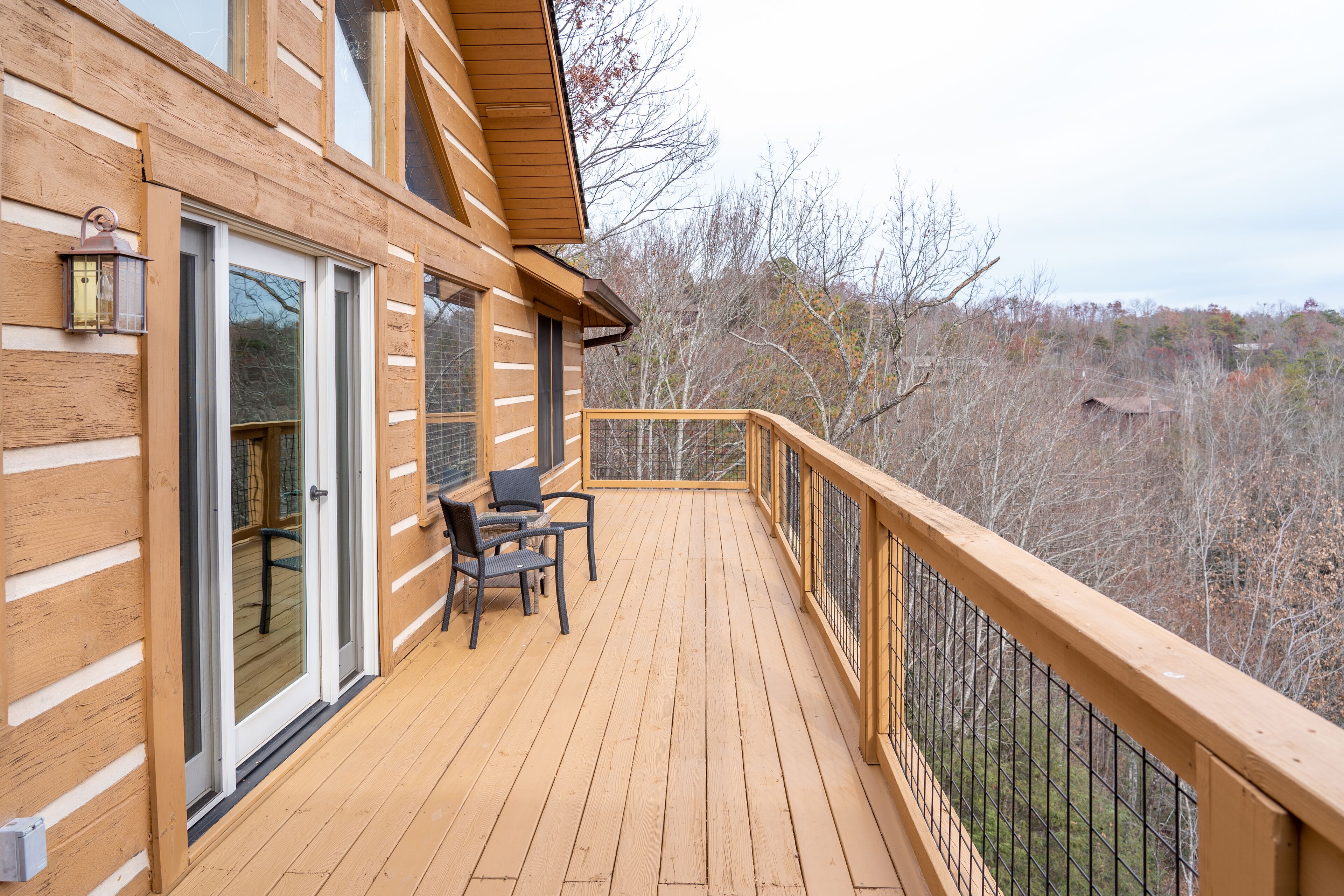 Une terrasse en bois avec une table et des chaises, une porte vitrée et une vue sur les arbres.