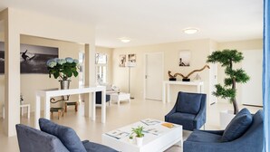 A modern living room with a white sofa, blue armchairs, a coffee table with magazines, and a potted plant.